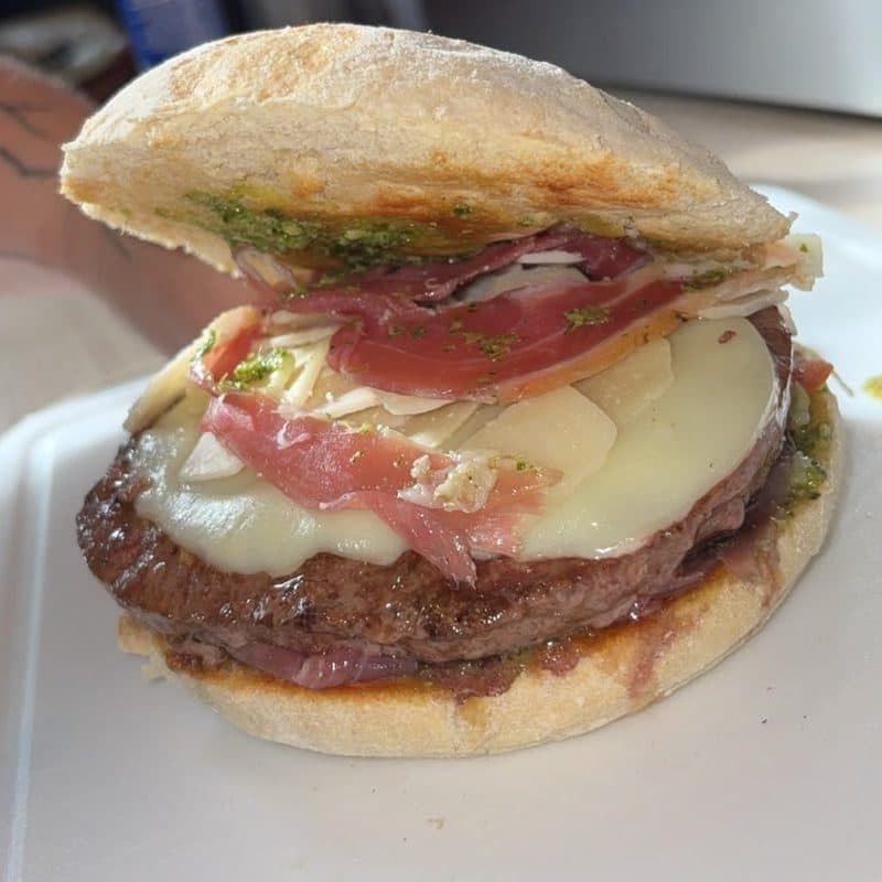 Le burger Le Charles Quint ouvert : viande pur bœuf, fromage fondu, jambon de Parme et pesto sur un pain fariné