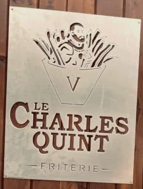 Plaque métallique gravée du logo Le Charles Quint Friterie, vissée sur le bardage en bois de la façade